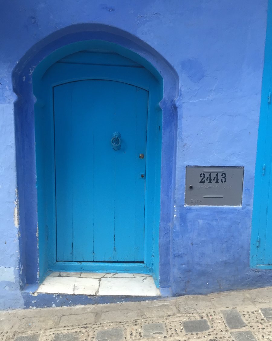 A turquoise door set in a keyhole arch on a blue-washed wall in the Chefchaouen medina