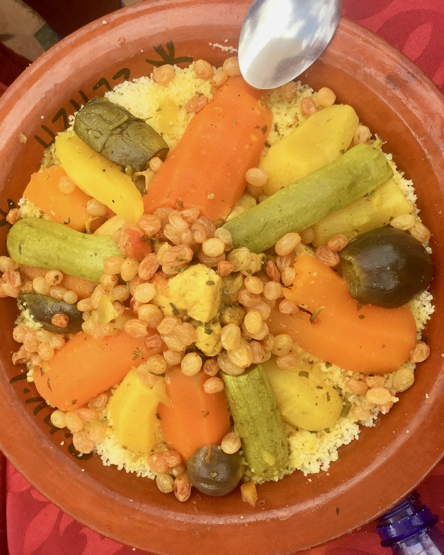 A wide earthenware dish of couscous ringed with carrots, courgettes, pumpkin and raisins